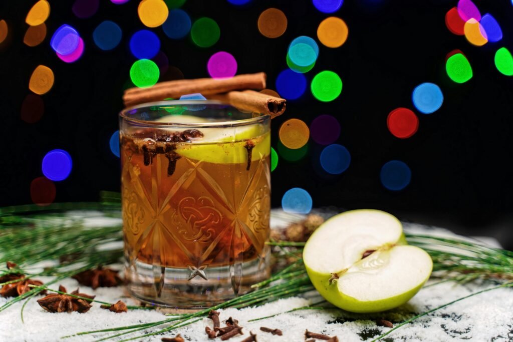 A festive cocktail with apples, cinnamon, and colorful lights, perfect for holiday celebrations.