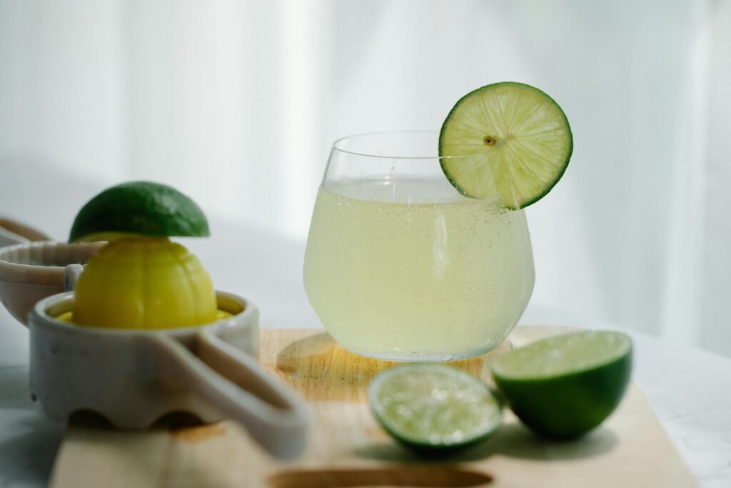 Close-up of a refreshing lime drink in a glass with fresh limes and a juicer on a wooden board.