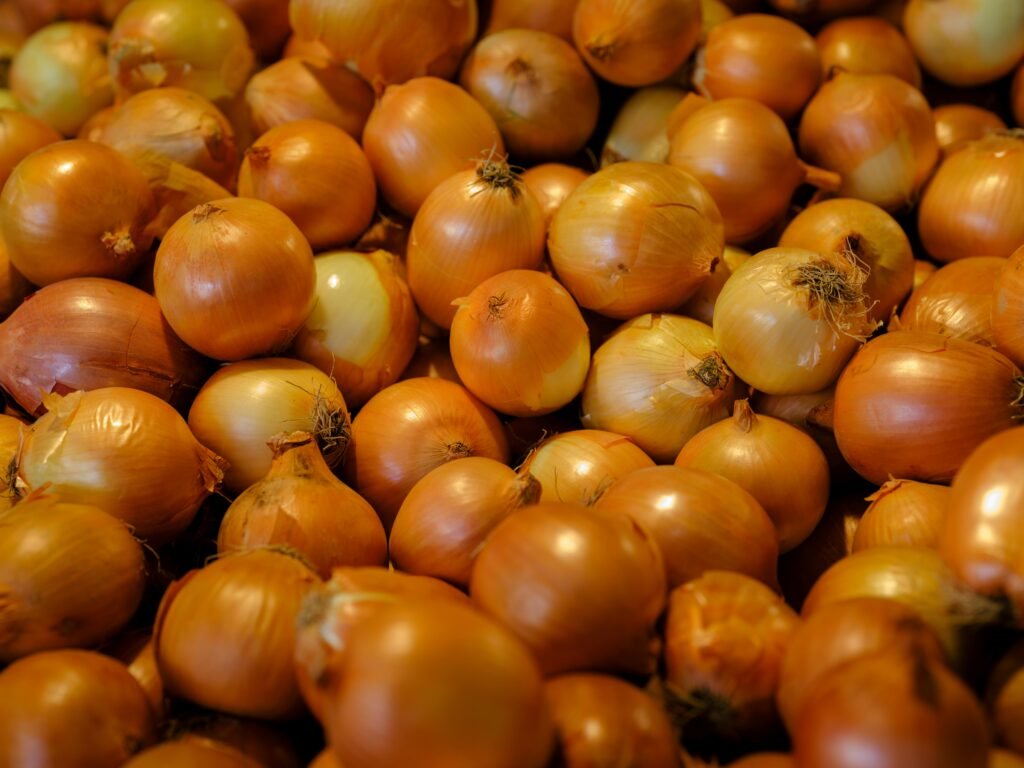 A pile of fresh, organic onions on display at a local farmers market showcasing their natural color and freshness.