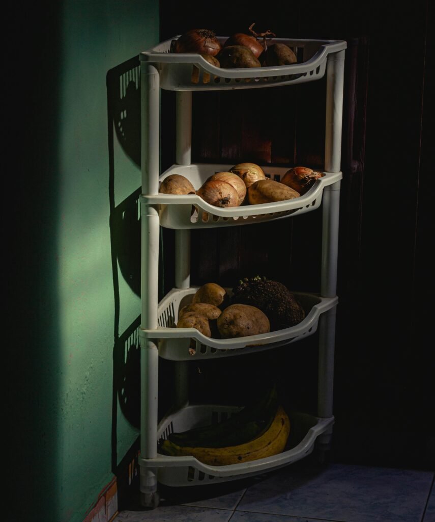 A shelf with vegetables and fruits casting shadows indoors, captured in sunlight.