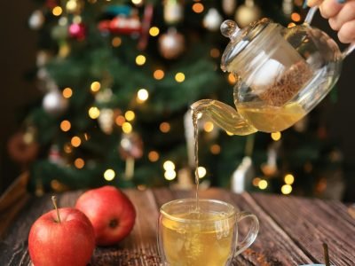 Warm winter tea being poured with apples and cinnamon in front of a decorated Christmas tree.